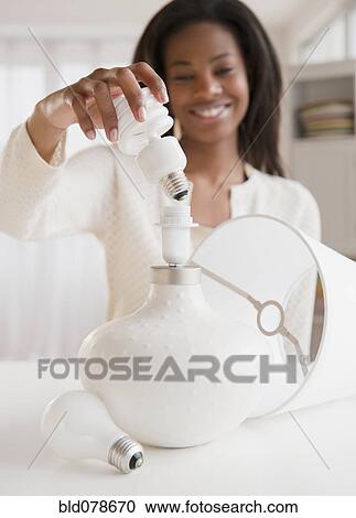 Stock Image - Mixed race woman putting cfl light bulb into lamp. Fotosearch
