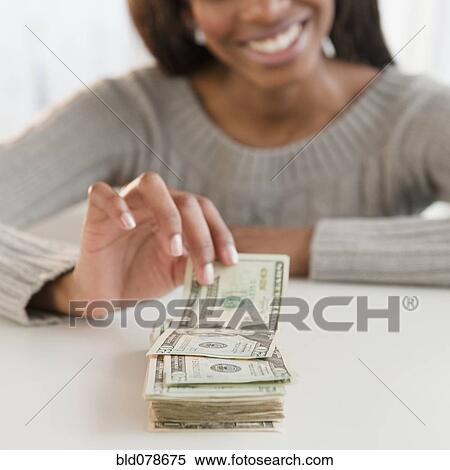 Stock Photography - Mixed race woman taking money from stack. Fotosearch