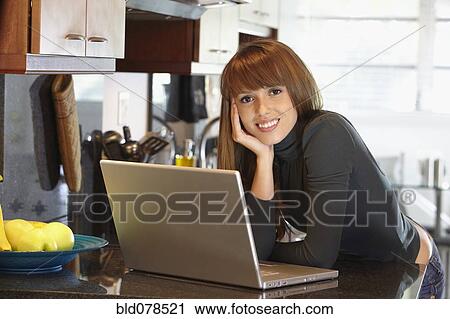Stock Image - Mixed race woman with laptop in kitchen. Fotosearch