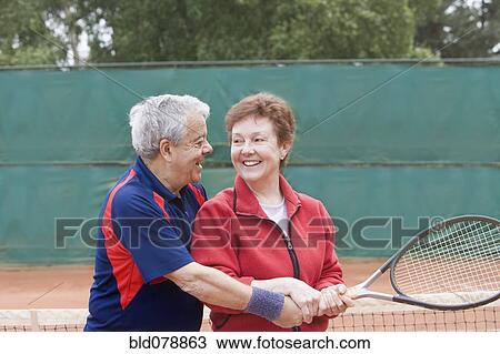 Stock Image - Senior Hispanic man teaching wife to play tennis. Fotosearch
