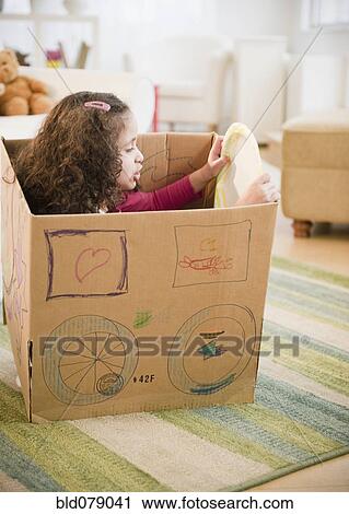 Stock Image - Hispanic girl playing in cardboard car. Fotosearch