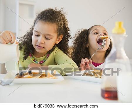Stock Image - Hispanic sisters eating pancakes. Fotosearch