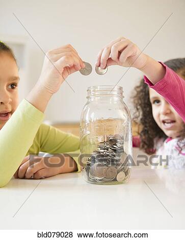 Stock Photo - Hispanic sisters putting coins in jar. Fotosearch