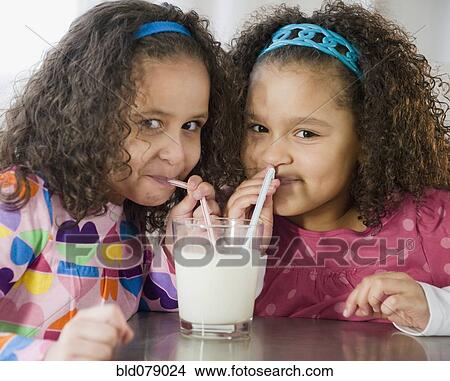Picture - Hispanic sisters sharing glass of milk. Fotosearch