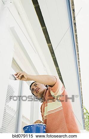 Stock Photography - Latin man painting outside of house. Fotosearch