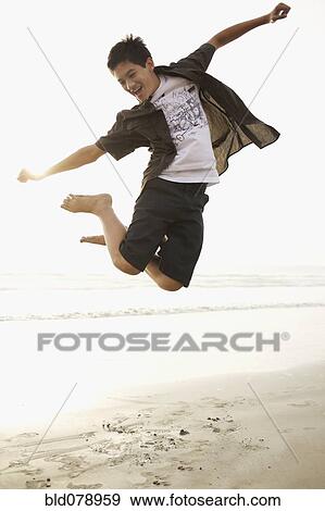 Stock Photo - Mixed race boy jumping on beach. Fotosearch