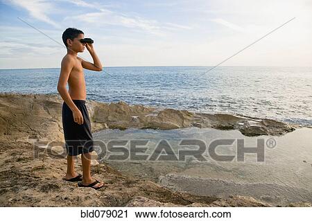 Stock Image - Mixed race boy looking at ocean with binoculars. Fotosearch