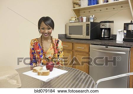 Picture - Mixed race businesswoman eating lunch in break room. Fotosearch
