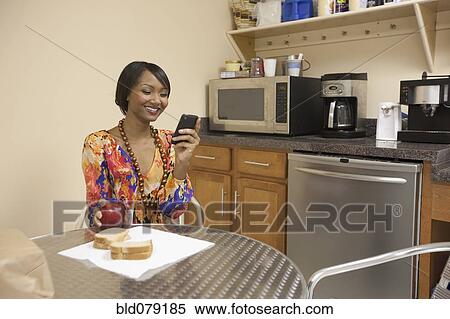 Stock Photography - Mixed race businesswoman eating lunch in break room. Fotosearch