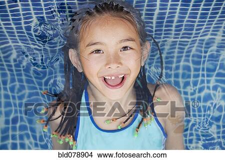 Picture - Mixed race girl floating in swimming pool. Fotosearch