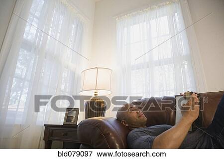 Stock Photo - Mixed race man laying on sofa reading book. Fotosearch