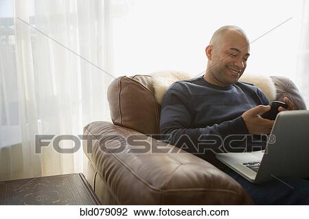 Stock Image - Mixed race man with laptop using cell phone. Fotosearch