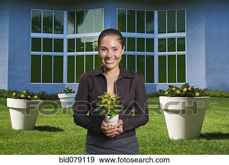 Stock Photo - Mixed race woman holding flowers in pot. Fotosearch