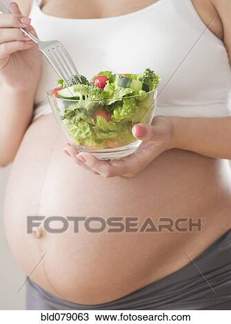 Stock Image - Pregnant Hispanic woman eating salad. Fotosearch
