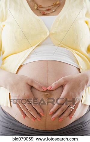 Pregnant Hispanic woman holding bare stomach View Large Photo Image Stock Photo - Pregnant Hispanic woman holding bare stomach. Fotosearch
