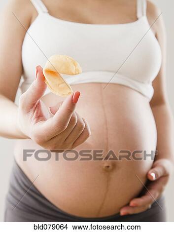 Picture - Pregnant Hispanic woman holding fortune cookie. Fotosearch
