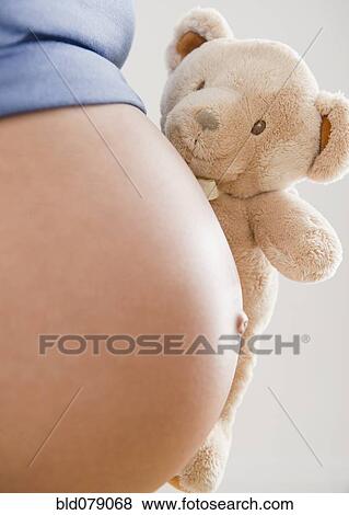 Stock Photo - Pregnant Hispanic woman holding teddy bear. Fotosearch