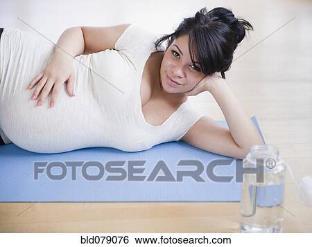 Stock Photograph - Pregnant Hispanic woman laying on yoga mat. Fotosearch