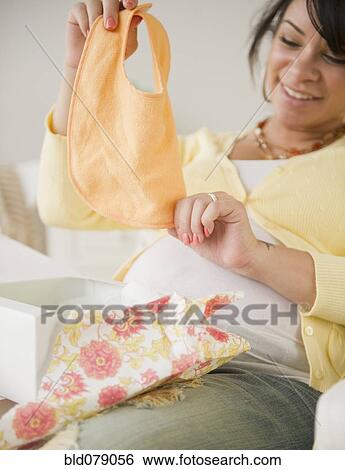 Stock Photograph - Pregnant Hispanic woman looking at baby bib. Fotosearch
