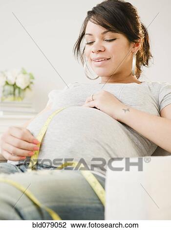 Stock Image - Pregnant Hispanic woman measuring stomach. Fotosearch
