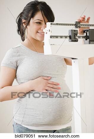 Stock Image - Pregnant Hispanic woman weighing herself. Fotosearch