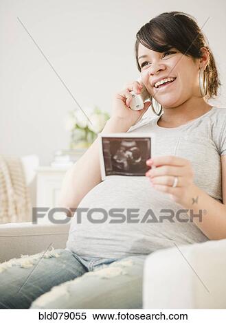 Stock Photography - Pregnant Hispanic woman with sonogram picture talking on phone. Fotosearch