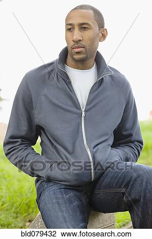 Stock Image - African American man sitting with hands in pockets. Fotosearch
