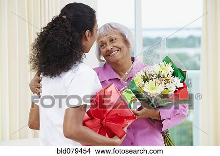 African American nurse giving senior woman flowers and gift View Large Photo Image Picture - African American nurse giving senior woman flowers and gift. Fotosearch
