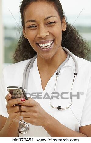 Stock Image - African American nurse text messaging on cell phone. Fotosearch