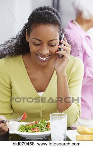 Stock Photo - African American woman eating salad and talking on cell phone. Fotosearch