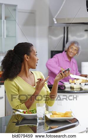 Stock Photo - African American woman eating salad and talking on cell phone. Fotosearch