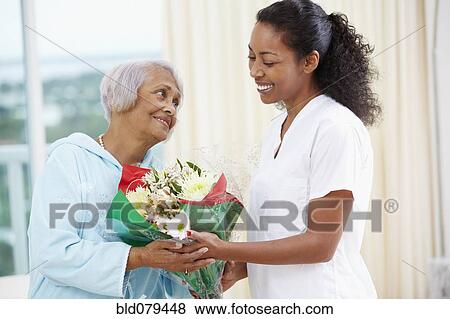 Stock Photo - African American woman giving nurse bouquet of flowers. Fotosearch