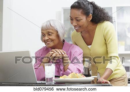 Stock Photograph - African American woman helping mother with laptop. Fotosearch