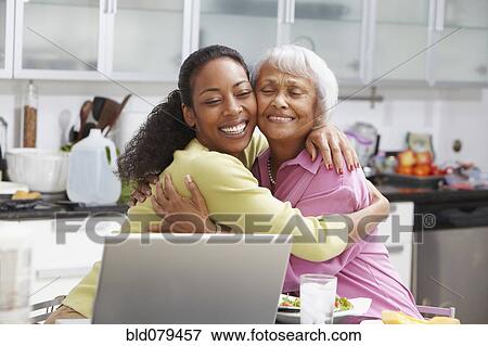 Stock Photo - African American woman hugging mother in kitchen. Fotosearch