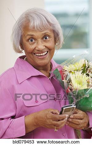 Stock Image - African American woman with bouquet text messaging on cell phone. Fotosearch