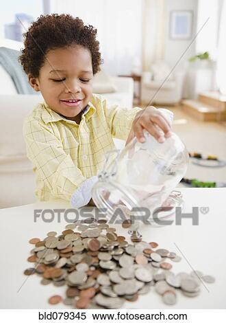 Stock Photography - Black boy emptying jar of coins on table. Fotosearch