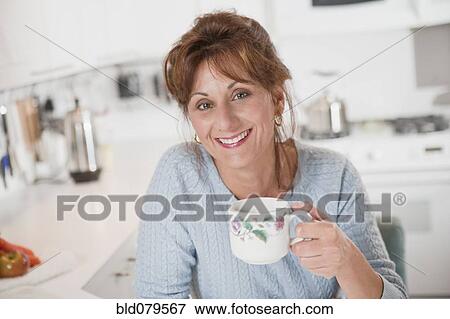 Caucasian woman drinking coffee in kitchen View Large Photo Image Stock Photo - Caucasian woman drinking coffee in kitchen. Fotosearch