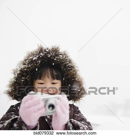 Stock Image - Chinese girl in snow using digital camera. Fotosearch