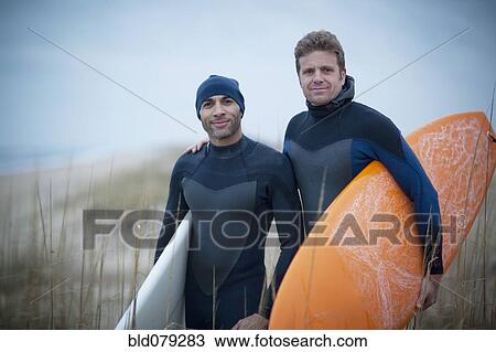 Stock Image - Men wearing wetsuits and carrying surfboards. Fotosearch