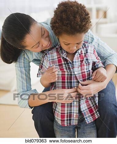 Stock Image - Mixed race mother helping son to dress. Fotosearch
