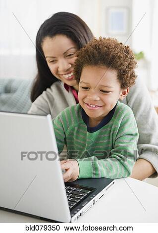 Stock Image - Mixed race mother using laptop with son. Fotosearch