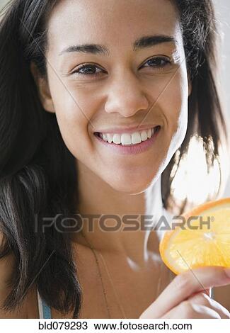 Stock Image - Mixed race woman holding orange slice. Fotosearch