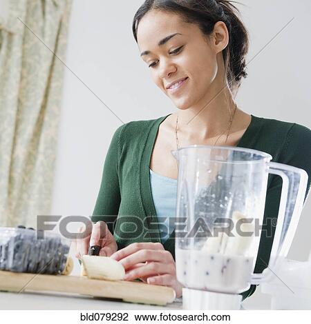 Stock Image - Mixed race woman preparing smoothie. Fotosearch