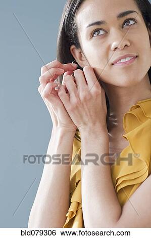 Stock Photograph - Mixed race woman putting on earrings. Fotosearch