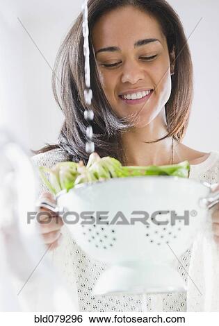Stock Photograph - Mixed race woman rinsing spinach. Fotosearch