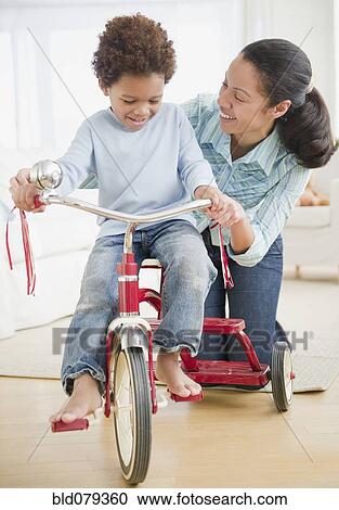 Mixed race woman teaching son to ride tricycle View Large Photo Image Stock Image - Mixed race woman teaching son to ride tricycle. Fotosearch