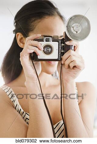 Stock Image - Mixed race woman using old-fashioned camera. Fotosearch