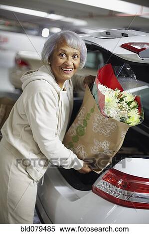 Stock Photography - Senior African American woman putting groceries into trunk of car. Fotosearch