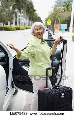 Stock Photo - Senior African American woman standing with car and luggage. Fotosearch