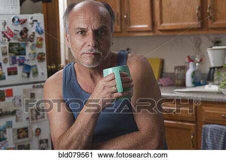 Stock Image - Serious Caucasian man drinking coffee in kitchen. Fotosearch
